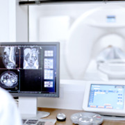 medico vendo laudo de ressonância magnética e paciente na máquina ao fundo