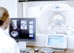 medico vendo laudo de ressonância magnética e paciente na máquina ao fundo