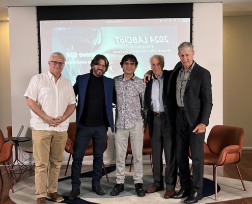 palestrantes em pé pousam para foto em palco de apresentação