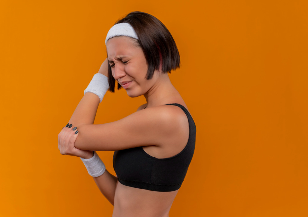 mulher atleta com expressão de dor, segurando o seu cotovelo