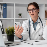 médica em consultório com celular na mão falando com paciente