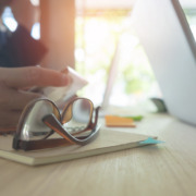 óculos em primeiro plano, sobre a mesa de escritório, com mãos de pessoas e notebook