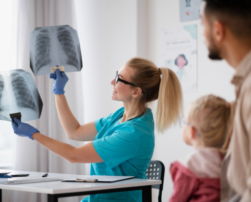 Médica radiologista mostra duas radiografias para pai e criança em consultório