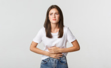 mulher de camiseta branca com expressão de dor e mãos na barriga