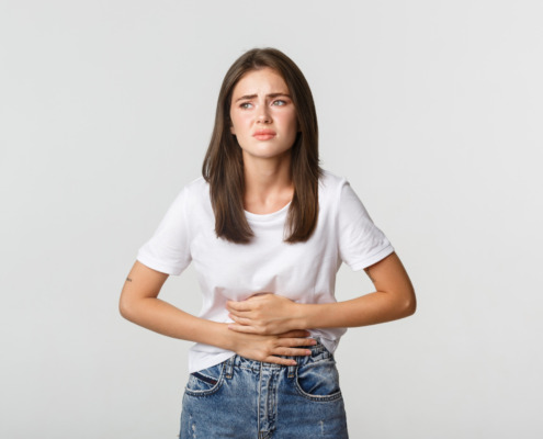 mulher de camiseta branca com expressão de dor e mãos na barriga