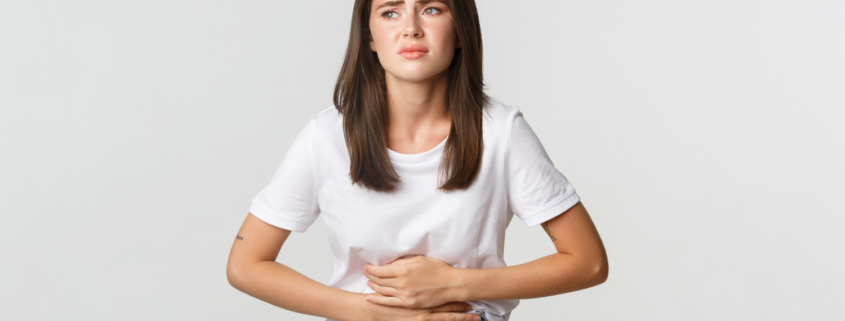 mulher de camiseta branca com expressão de dor e mãos na barriga