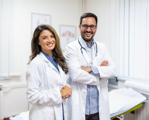 casal de médicos sorrindo e braços cruzados em ambiente hospitalar