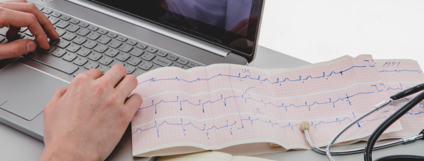 notebook na bancada com exame de eletrocardiograma ao lado