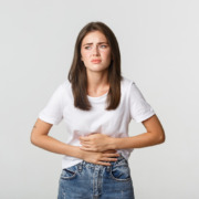 mulher de camiseta branca e calça jeans, com mão na barriga e rosto de dor