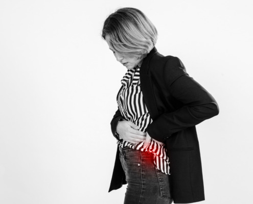 Mulher de perfil com mão na barriga e uma mancha vermelha simulando ponto da dor na barriga