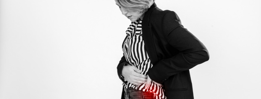 Mulher de perfil com mão na barriga e uma mancha vermelha simulando ponto da dor na barriga