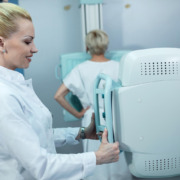 médica em pé realizando exame de mamografia em paciente ao fundo
