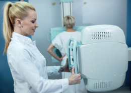 médica em pé realizando exame de mamografia em paciente ao fundo