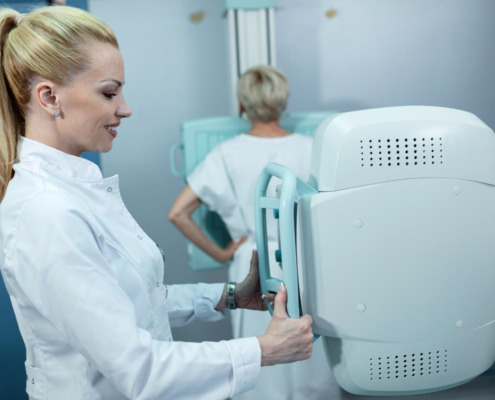 médica em pé realizando exame de mamografia em paciente ao fundo