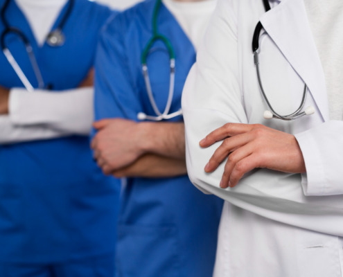 Corpo de três médicos sendo um com jaleco branco e dois com jalecos azuis