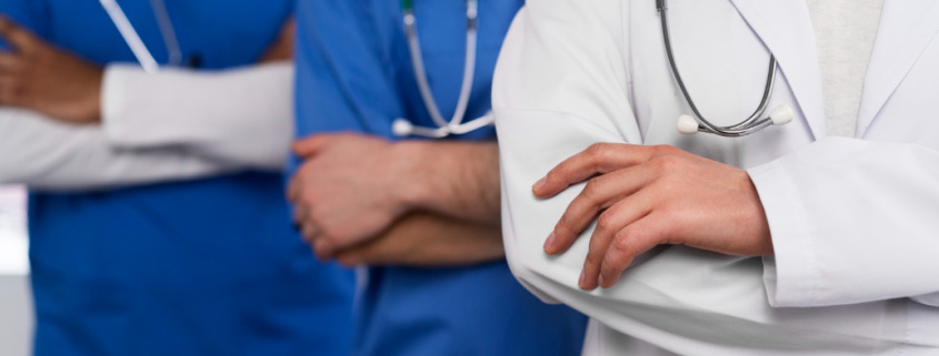 Corpo de três médicos sendo um com jaleco branco e dois com jalecos azuis