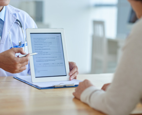 médico no consultório mostrando tela do tablet com formulário para paciente