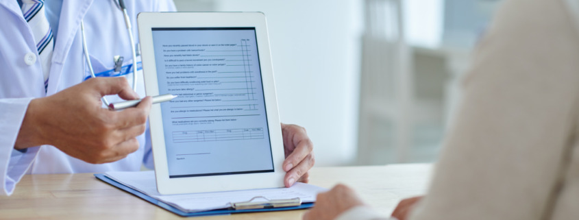 médico no consultório mostrando tela do tablet com formulário para paciente