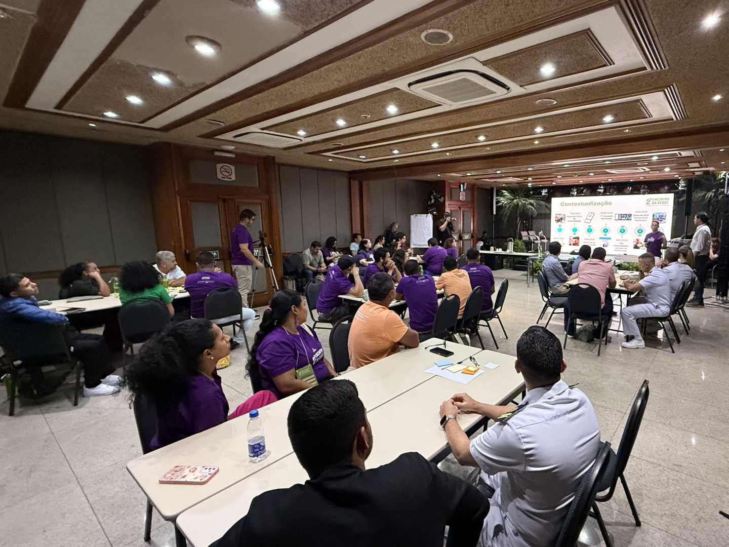 pessoas reunidas em sala de reunião com telão ao fundo