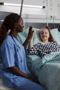 enfermeira de jaleco azul cumprimenta criança em cama de hospital