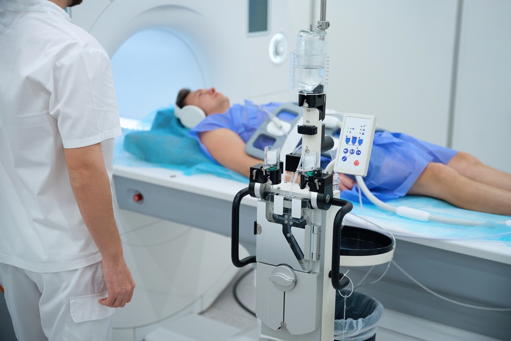 paciente com avental azul, protetor de ouvido, deitado em máquina de ressonância magnética