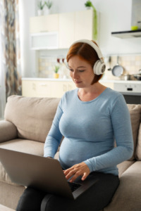 mulher grávida sentada no sofá em consulta por telemedicina com notebook
