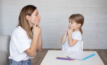 mãe e filha fazendo treinamento de fala com caderno e caneta a mesa
