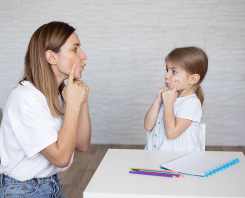 mãe e filha fazendo treinamento de fala com caderno e caneta a mesa
