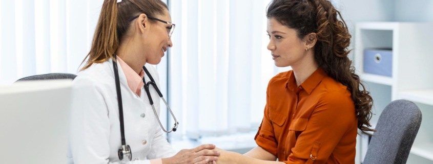 médica em consultório segura a mão de paciente e conversam