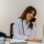 médica em consultório de jaleco branco falando ao telefone