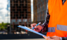 técnico de segurança com coleta laranja e prancheta na mão