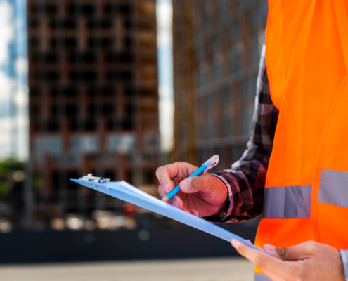 técnico de segurança com coleta laranja e prancheta na mão