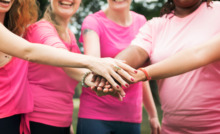 mulheres em pé, em área aberta, com camisetas rosa e colocando uma mão sobre a outra