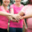 mulheres em pé, em área aberta, com camisetas rosa e colocando uma mão sobre a outra