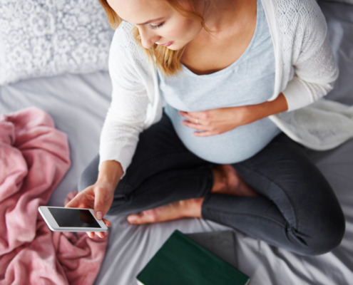 mulher gestante na cama olhando tela do celular