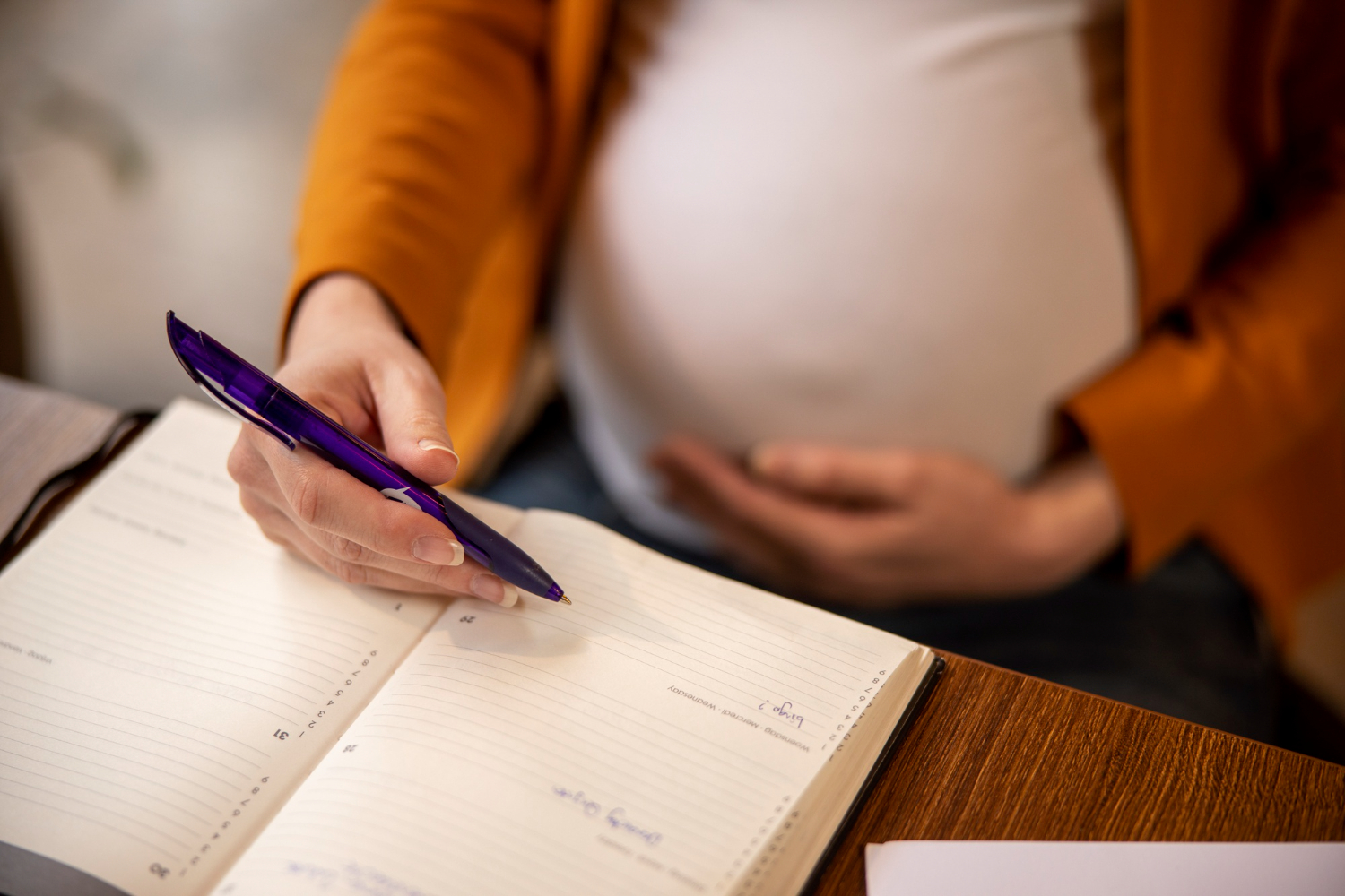 mulher gestante com mão na barriga, sentada e com bloco de notas a frente