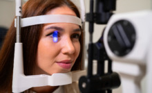 mulher apoia o rosto em aparelho oftalmológico com luz azul no olho direito