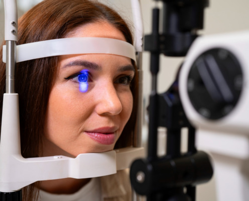 mulher apoia o rosto em aparelho oftalmológico com luz azul no olho direito