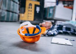 homem caído no chão com capacete de EPI ao lado