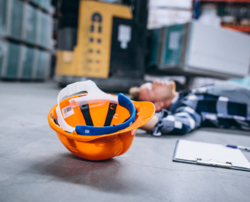 homem caído no chão com capacete de EPI ao lado