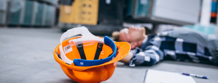 homem caído no chão com capacete de EPI ao lado