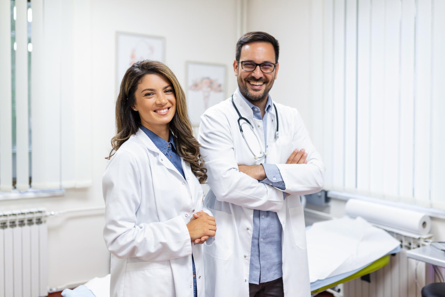 médico e médica em pé, em consultório, sorrindo