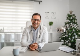 médico em consultório sorrindo e com notebook na mesa