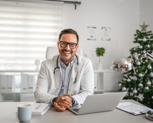 médico em consultório sorrindo e com notebook na mesa