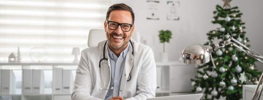 médico em consultório sorrindo e com notebook na mesa