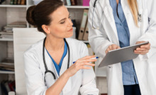 médica com jaleco branco vendo tablet com outra médica em consultório