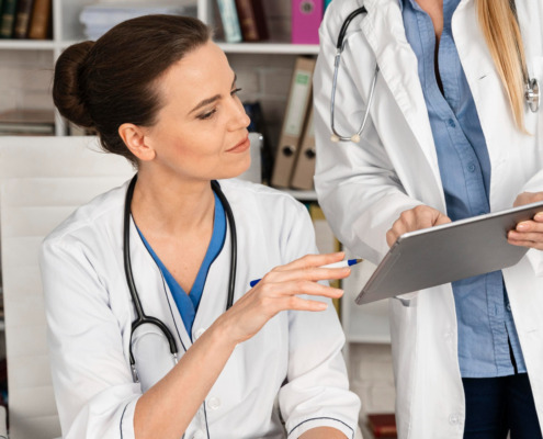 médica com jaleco branco vendo tablet com outra médica em consultório