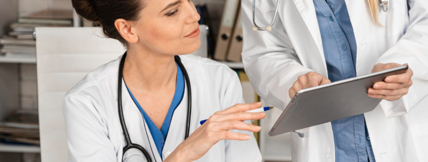 médica com jaleco branco vendo tablet com outra médica em consultório