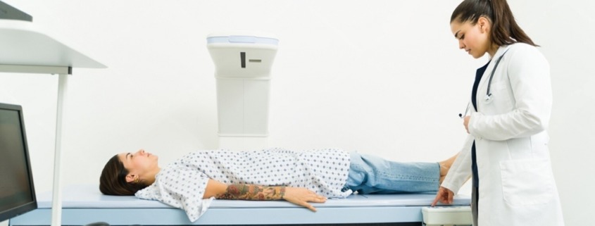 ´paciente deitada em máquina de desitometria óssea com médica ao lado