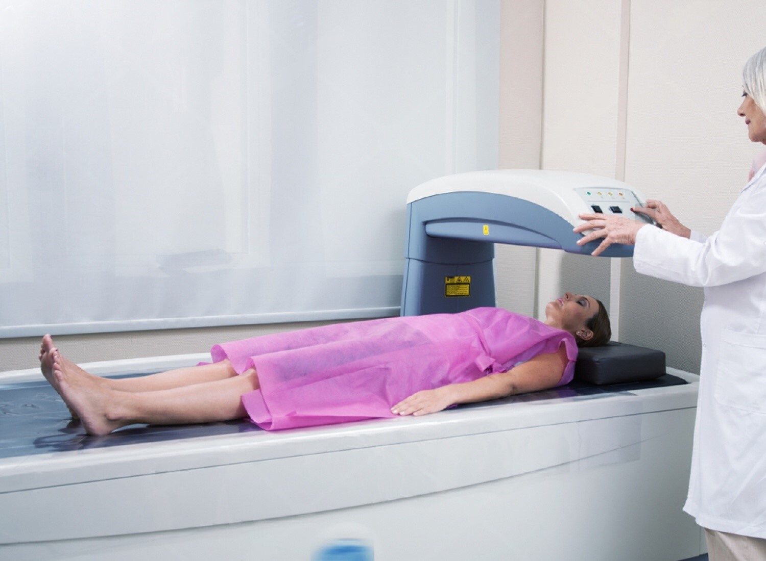 paciente deitada em máquina de desitometria com médica auxiliando